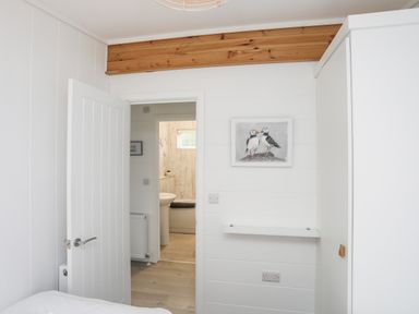 A bedroom with a partially open door leading to a bathroom a wall shelf and a painting of two birds at Galwad y Mor in Niwbwrch newborough