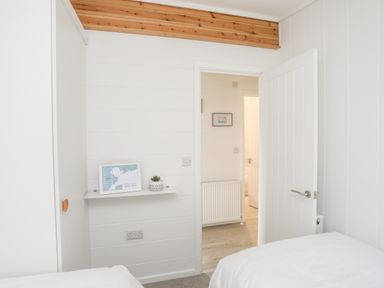 A bedroom with two beds a white door a small shelf with a framed picture and a plant at Galwad y Mor in Niwbwrch newborough