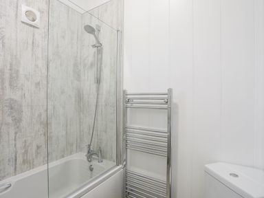 A bathroom with a bathtub shower and a chrome towel radiator at Galwad y Mor in Niwbwrch newborough