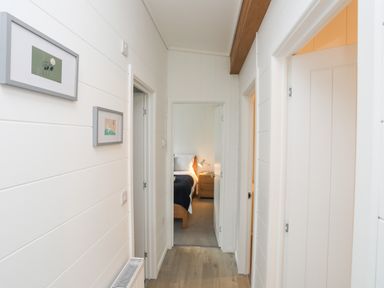 A hallway with doors leading to rooms and framed pictures on the walls at Galwad y Mor in Niwbwrch