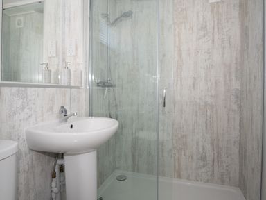 A bathroom with a sink a mirror soap dispenser and a shower at Galwad y Mor in Niwbwrch newborough