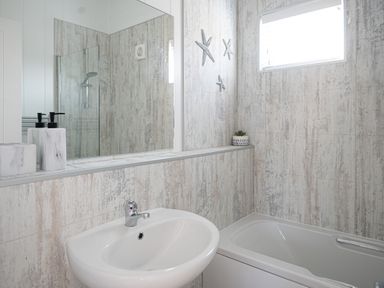 A bathroom with a sink a bathtub a large mirror and starfish wall decorations at Galwad y Mor in Niwbwrch newborough