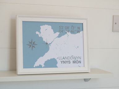 A framed map with coordinates on a white shelf at Galwad y Mor in Niwbwrch (newborough)