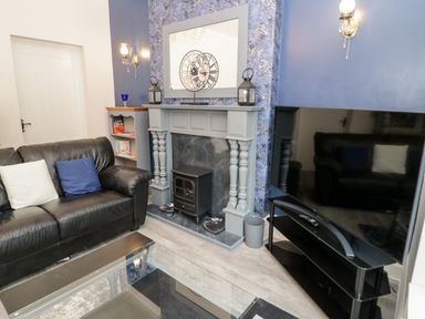 A living room with a black leather sofa a fireplace with a clock on the mantel and a television on a black stand at Gwyder in Penmaenmawr