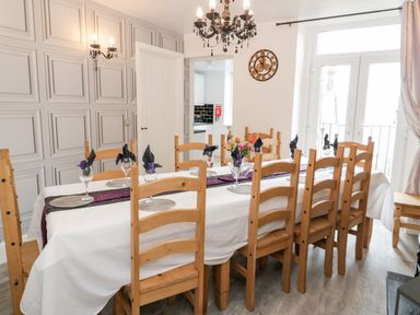 A dining room with a long table set with glasses and napkins surrounded by wooden chairs at Gwyder in Penmaenmawr
