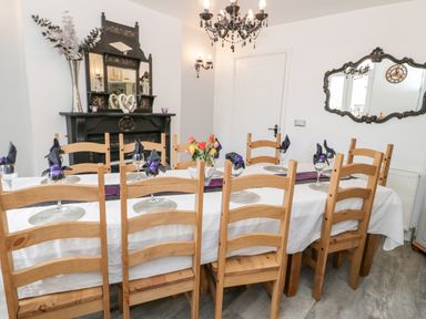 A dining room with a long table set with glasses and napkins surrounded by wooden chairs and a black fireplace in the background at Gwyder in Penmaenmawr