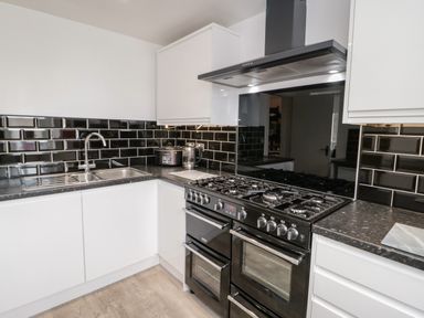 A kitchen with white cabinets black countertops black tiled backsplash a sink and a black stove at Gwyder Penmaenmawr