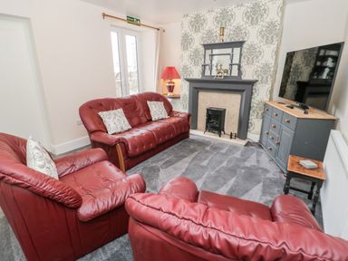 A living room with red leather sofas a fireplace with decorative items a television on a cabinet and a table lamp at Gwyder in Penmaenmawr