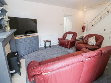 A living room with red leather sofas a grey cabinet with a television and a fireplace at Gwyder in Penmaenmawr