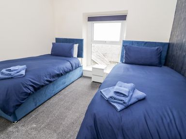 A bedroom with two single beds with blue bedding and towels on each bed at Gwyder in Penmaenmawr