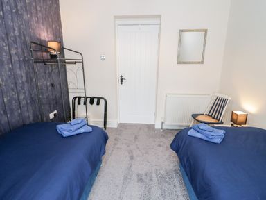 A bedroom with two single beds with blue bedding and towels on a chair and clothing rack at Gwyder in Penmaenmawr