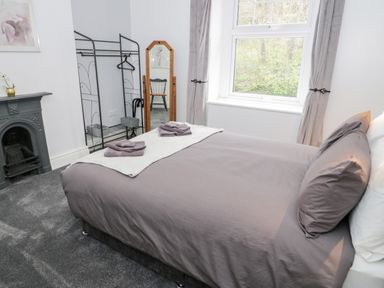 A bedroom with a bed covered in gray bedding and towels on top near a window with gray curtains and a black fireplace at Gwyder in Penmaenmawr