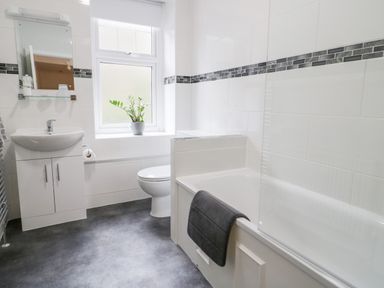 A bathroom with a sink, mirror, toilet, bathtub with a towel, and a window with a plant at Gwyder in Penmaenmawr