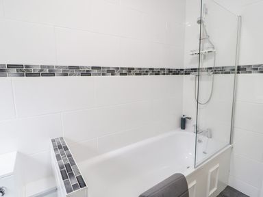 A bathroom with a bathtub shower and tiled walls at Gwyder in Penmaenmawr