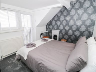 A bedroom with a bed and folded towels near a window with blinds and radiator at Gwyder in Penmaenmawr