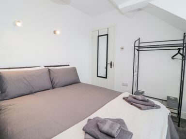 A bedroom with a double bed brown bedding wall-mounted lights a door with a mirror and a black metal clothes rack at Gwyder in Penmaenmawr