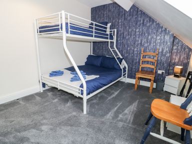A bedroom with a white metal bunk bed with blue bedding and towels a wooden chair a small white bedside table with a lamp and a blue patterned wall at Gwyder in Penmaenmawr