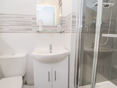 A bathroom with a toilet, sink with cabinet, mirror, and glass-enclosed shower at Gwyder in Penmaenmawr