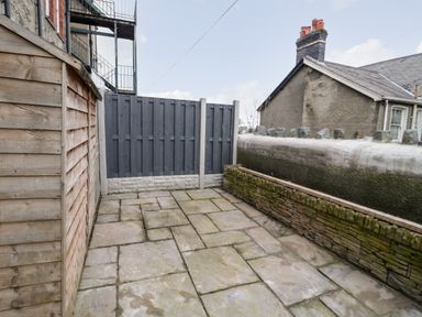 A small paved outdoor area with a wooden shed dark grey fence and stone wall at Gwyder in Penmaenmawr