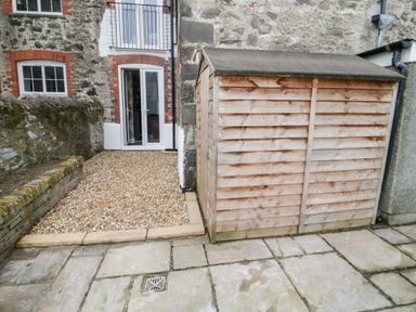 A stone-paved courtyard with a wooden shed and a gravel area leading to a door with white frames at Gwyder in Penmaenmawr