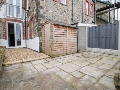A small paved courtyard with a wooden shed next to a stone building at Gwyder in Penmaenmawr