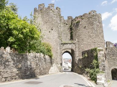 A stone medieval castle entrance with an arched gateway and surrounding stone walls with greenery in Penmaenmawr