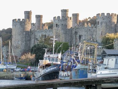 A harbor with boats docked in front of a medieval stone castle at Gwyder in Penmaenmawr