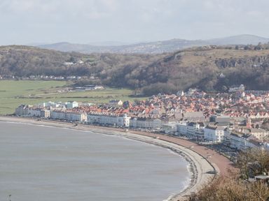 A coastal town with a curved beach and a promenade lined with buildings near green hills at Gwyder in Penmaenmawr