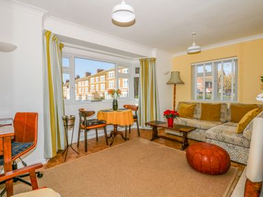 A living room with a patterned sofa and mustard cushions a wooden coffee table and a red pouf at See The Sea in Hunstanton