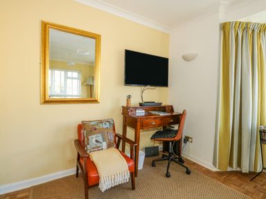 A corner with a wooden desk and chair under a wall-mounted TV and an armchair with cushion and throw at See The Sea in Hunstanton