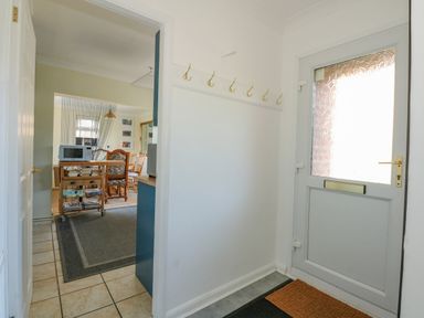 A hallway with coat hooks and a door next to a dining area with chairs and a microwave at See The Sea in Hunstanton