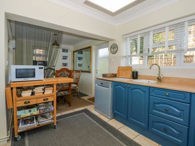 A kitchen with blue cabinets a wooden countertop a sink and dishwasher next to a wooden trolley with a microwave and books at See The Sea Hunstanton