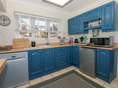 A kitchen with blue cabinets dishwasher microwave and a window with blinds at See The Sea in Hunstanton