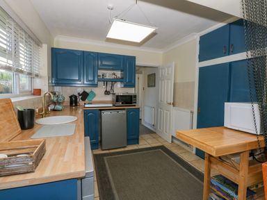 A kitchen with blue cabinets a wooden countertop a sink a microwave and a small refrigerator at See The Sea Hunstanton
