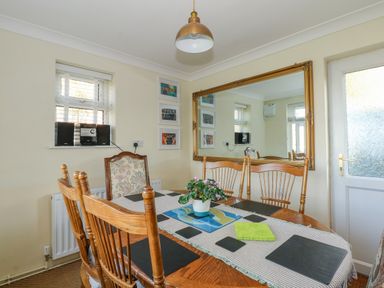A dining room with wooden chairs a table with placemats a plant and a large mirror on the wall at See The Sea in Hunstanton
