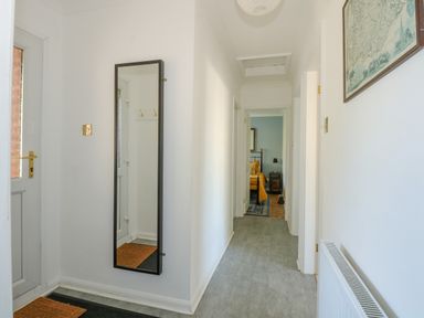 A hallway with a full-length mirror on the wall a door with a glass panel and a view of a bedroom at See The Sea in Hunstanton