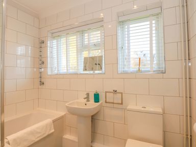 A bathroom with a bathtub towel sink soap dispenser toilet and two windows with blinds at See The Sea in Hunstanton