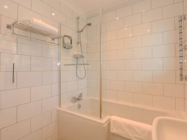 A bathroom with a bathtub shower and towel rack at See The Sea in Hunstanton