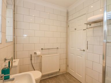 A bathroom with a toilet sink radiator a door and towel rack at See The Sea in Hunstanton