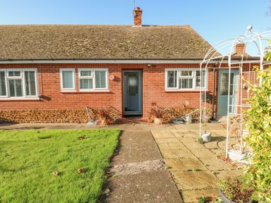 Front exterior view of a brick bungalow with a pathway leading to blue doors and a small garden area with grass at See The Sea in Hunstanton