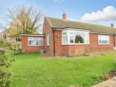A single story brick house with a large window and green lawn at See The Sea in Hunstanton