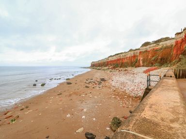A sandy beach with scattered rocks and red cliffs alongside the sea at See The Sea in Hunstanton