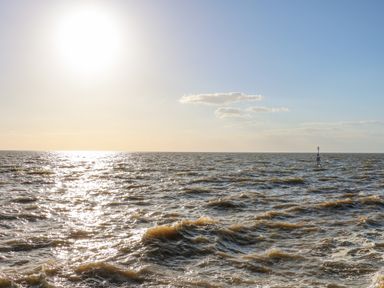A large body of water with waves and a navigation marker under a bright sun at See The Sea in Hunstanton