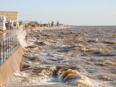 A waterfront with waves hitting a sea wall and people walking along a promenade at See The Sea in Hunstanton