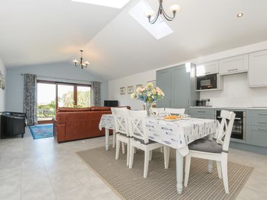 A kitchen dining area with a table and chairs and a sitting room with sofas and a television at Lambley View in Bude