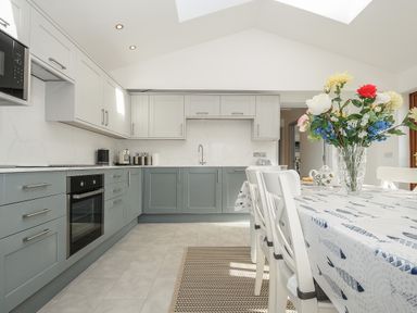 A kitchen with blue and white cabinets a dining table with chairs and a vase of flowers at Lambley View in Bude