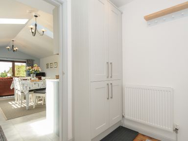 A hallway with white cabinets and a radiator looking into a dining area with a table set and chairs at Lambley View in Bude
