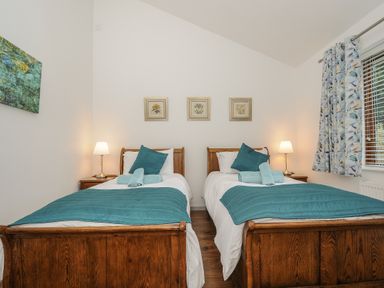 A bedroom with two single wooden beds with teal blankets and pillows and bedside tables with lamps at Lambley View in Bude