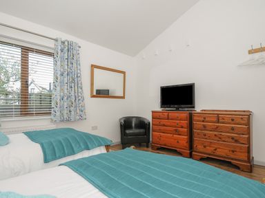 A bedroom with two single beds a black armchair a TV on two wooden dressers and a window with curtains at Lambley View in Bude