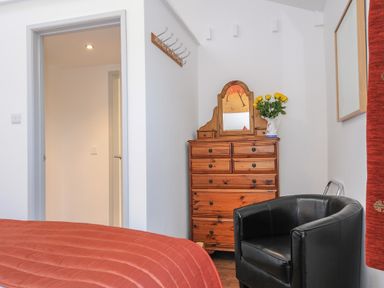 A bedroom corner with a wooden dresser and mirror a black chair and a bed with a red quilt at Lambley View in Bude